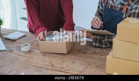 Ein paar Inhaber eines kleinen Unternehmens, die am Arbeitsplatz mit Computern arbeiten. Ein Geschäftsmann prüft die Produktbestellung. Verpacken von Waren für die Lieferung an den Kunden Stockfoto