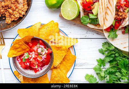 Tacos mit Rindfleisch, Mais, roten Bohnen und roten Zwiebeln in Maistortilla und Nachos mit Salsa auf dem Teller. Mexikanische Küche. Weißer Tischhintergrund, Draufsicht Stockfoto