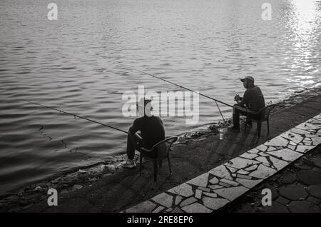 Zwei vietnamesische Männer sitzen im Reunification Park im Zentrum von Hanoi, Vietnam, und fischen bei Sonnenuntergang im See. Stockfoto