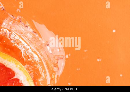 Nahaufnahme einer roten Grapefruitscheibe im Wasser mit Kopierbereich auf orangefarbenem Hintergrund Stockfoto