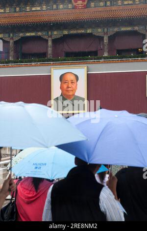 Chinesische Touristen, die die Verbotene Stadt verlassen und sich an einem nassen Tag mit Sonnenschirmen vor Regen schützen, auf dem Platz des Himmlischen Friedens, Peking, China. Porträt des Vorsitzenden Mao Tse Tung sieht von der Wand aus. (125) Stockfoto