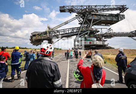 26. Juli 2023, Sachsen, Groitzsch: Zahlreiche Zuschauer folgen einem Bagger mit Schaufelrädern „SRS 1300“, der vom Tagebau Schleenhain auf die Bundesautobahn 176 zum ca. 10 km entfernten Bergbaufeld Peres fährt. Die Maschine, die gut 1680 Tonnen wiegt, bewegt sich und wird ab dem Herbst weiterhin für den Braunkohlebergbau eingesetzt. Nach Angaben der Mitteldeutschen Braunkohlengesellschaft (Mibrag) ist der Bagger seit Juli 12 in Bewegung und wird am nächsten Montag am Zielort ankommen. Zum Schutz der Fahrbahn wurde die Straße mit Planen, Bändern und einer Schicht o abgedeckt Stockfoto