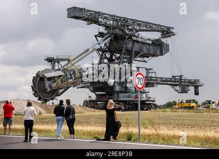 26. Juli 2023, Sachsen, Groitzsch: Zahlreiche Zuschauer folgen einem Bagger mit Schaufelrädern „SRS 1300“, der vom Tagebau Schleenhain auf die Bundesautobahn 176 zum ca. 10 km entfernten Bergbaufeld Peres fährt. Die Maschine, die gut 1680 Tonnen wiegt, bewegt sich und wird ab dem Herbst weiterhin für den Braunkohlebergbau eingesetzt. Nach Angaben der Mitteldeutschen Braunkohlengesellschaft (Mibrag) ist der Bagger seit Juli 12 in Bewegung und wird am nächsten Montag am Zielort ankommen. Zum Schutz der Fahrbahn wurde die Straße mit Planen, Bändern und einer Schicht o abgedeckt Stockfoto