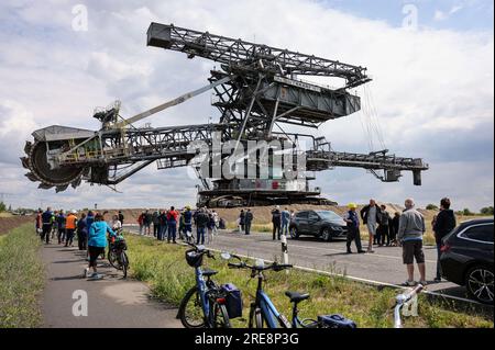 26. Juli 2023, Sachsen, Groitzsch: Zahlreiche Zuschauer folgen einem Bagger mit Schaufelrädern „SRS 1300“, der vom Tagebau Schleenhain auf die Bundesautobahn 176 zum ca. 10 km entfernten Bergbaufeld Peres fährt. Die Maschine, die gut 1680 Tonnen wiegt, bewegt sich und wird ab dem Herbst weiterhin für den Braunkohlebergbau eingesetzt. Nach Angaben der Mitteldeutschen Braunkohlengesellschaft (Mibrag) ist der Bagger seit Juli 12 in Bewegung und wird am nächsten Montag am Zielort ankommen. Zum Schutz der Fahrbahn wurde die Straße mit Planen, Bändern und einer Schicht o abgedeckt Stockfoto