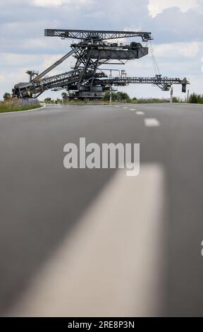 26. Juli 2023, Sachsen, Groitzsch: Ein Schaufelbagger „SRS 1300“ überquert die Bundesautobahn 176 auf dem Weg vom Tagebau Schleenhain zum ca. 10 km entfernten Bergbaufeld Peres. Die Maschine, die gut 1680 Tonnen wiegt, bewegt sich und wird ab dem Herbst weiterhin für den Braunkohlebergbau eingesetzt. Nach Angaben der Mitteldeutschen Braunkohlengesellschaft (Mibrag) ist der Bagger seit Juli 12 in Bewegung und wird am nächsten Montag am Zielort ankommen. Zum Schutz der Straße wurde die Straße mit Planen, Klebebändern und einer Schicht Kiessandmischung abgedeckt Stockfoto