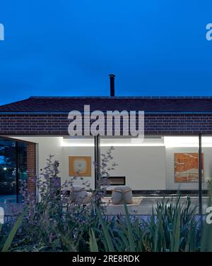 Blick vom Garten bis zum Wohnbereich in der Dämmerung. Gelistetes Farmstead, Suffolk, Vereinigtes Königreich. Architekt: Rodic Davidson Architects, 2021. Stockfoto