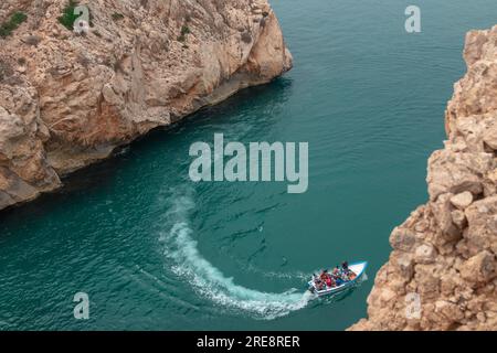 Ein Blick von oben auf ein Boot, das zwischen zwei großen felsigen Bergen an einem der Strände der Stadt El Jebha, Marokko, fährt Stockfoto