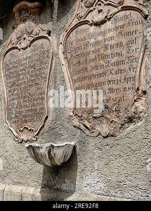 Zwei antike Marmorgräber aus dem 18. Jahrhundert mit Inschrift in altdeutscher Sprache und ein an der Außenwand des Ren eingehaustes Weihwasser-Becken Stockfoto
