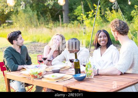 Familie und multiethnische, vielfältige Freunde treffen sich an einem Gartentisch. Leute essen gegrilltes und frisches Gemüse, teilen leckere Salate für eine große Familienfeier mit Verwandten. Hochwertiges Foto Stockfoto