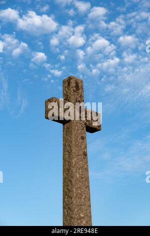 Blick aus dem niedrigen Winkel auf ein uraltes Steinkreuz unter einem hellblauen Himmel in Erinnerung an die Toten und repräsentiert Hoffnung, Tod und Trauer Stockfoto