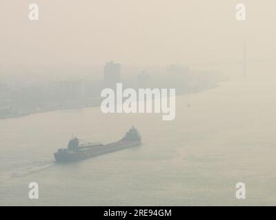 Ein Frachtfrachter navigiert durch den Waldbrandrauch Kanadas auf dem Detroit River, als er sich der Kanada-US-Grenze nähert, die die Ambassador Bridge überquert Stockfoto