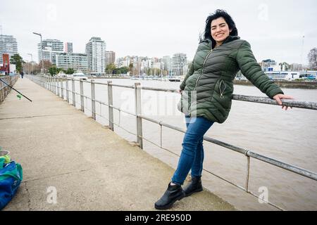 Junge Latina-Frau venezolanischer ethnischer Herkunft in einer grünen Jacke und blauen jeans-Hosen, steht und lehnt sich an das Geländer der Brücke, ruht auf Visiti Stockfoto