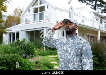 afroamerikanischer Soldat in Militäruniform, salutiert und bleibt gegen das Haus Stockfoto