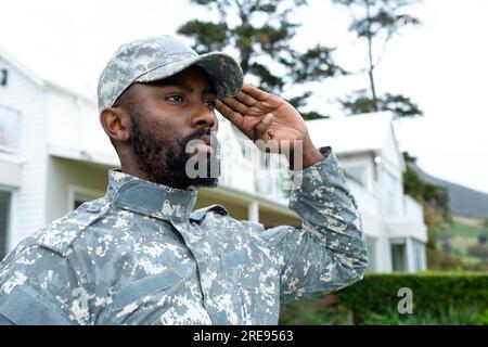 afroamerikanischer Soldat in Militäruniform, salutiert und bleibt gegen das Haus Stockfoto