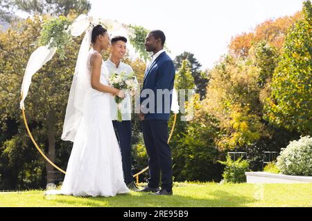 Fröhlicher, vielseitiger Beamter, Braut und Bräutigam bei einer Hochzeit im Freien im sonnigen Garten, Kopierbereich Stockfoto