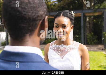 Frohe afroamerikanische Braut und Bräutigam bei der Hochzeitszeremonie im sonnigen Garten Stockfoto