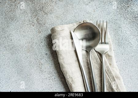 Besteckset auf grauer Oberfläche neben einem rauen, strukturierten Hintergrund mit Handtuchserviette und trockenem Löffel in einer leichten Küche Stockfoto