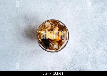 Blick von oben auf einen transparenten Glasbecher mit Whiskey-alkoholischem Getränk und einen Cocktail aus Oliven mit Eiswürfeln auf grauem Hintergrund im Studio Stockfoto