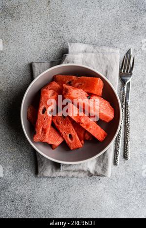 Von oben geschnittene Stücke Wassermelone in der Schüssel auf Tischdecke mit Besteck auf Betonhintergrund an der Seite Stockfoto