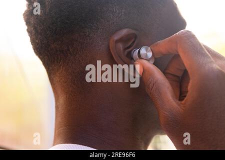 Nahaufnahme von außen: Abgeschnittener, nicht wiedererkennbarer junger afroamerikanischer Mann, der echte kabellose Kopfhörer trägt und draußen Musik hört Stockfoto