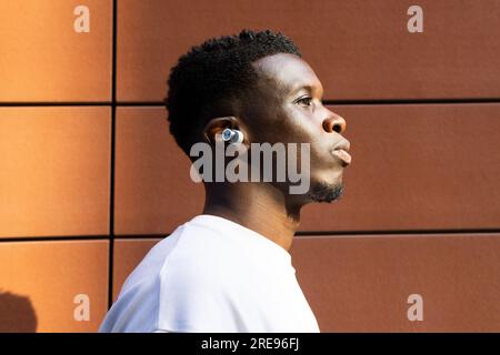 Porträtansicht eines männlichen afroamerikanischen Mannes in einem weißen T-Shirt, der wegschaut, während er an der orangefarbenen Wand steht Stockfoto