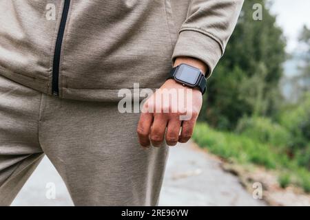 Anonyme Person in Sportbekleidung mit einer Digitaluhr am Handgelenk, die auf einer Landstraße steht. Stockfoto