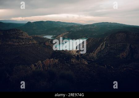 Malerischer Blick auf die Landschaft mit felsigen Bergen und grünen Tälern mit Bäumen, wilden Sträuchern, während Sie den ruhigen blauen See unter bewölktem Himmel i des Sonnenuntergangs umgeben Stockfoto