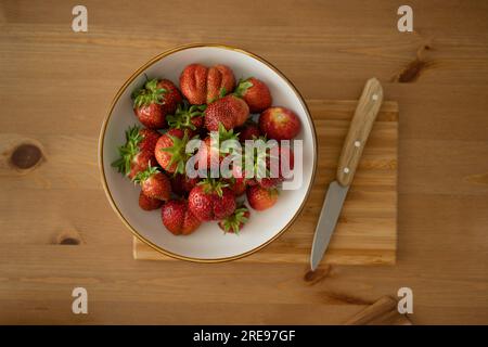 Draufsicht auf frische Erdbeeren in Schüssel und Messer auf Holzbrett über Holztisch bei Tageslicht Stockfoto