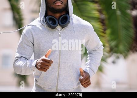 Ein anonymer junger afroamerikanischer Mann mit Bart in Sportbekleidung, während er auf der Straße auf unscharfem Hintergrund läuft Stockfoto