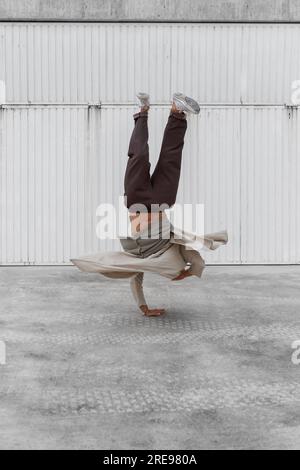 Nicht erkennbarer männlicher Tänzer, der Breakdance-Bewegungen zeigt, während er auf den Armen balanciert Und die Durchführung von Handhopps auf Betonboden im Stadtgebiet Stockfoto