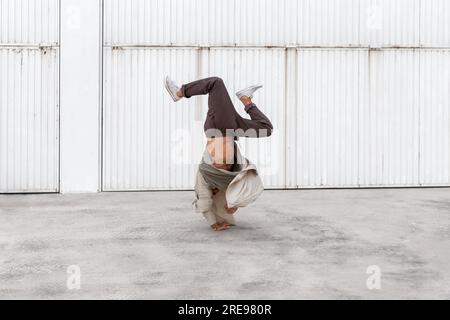 Nicht erkennbarer männlicher Tänzer, der Breakdance-Bewegungen zeigt, während er auf den Armen balanciert Und die Durchführung von Handhopps auf Betonboden im Stadtgebiet Stockfoto