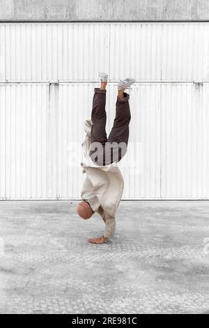 Nicht erkennbarer männlicher Tänzer, der Breakdance-Bewegungen zeigt, während er auf den Armen balanciert Und die Durchführung von Handhopps auf Betonboden im Stadtgebiet Stockfoto