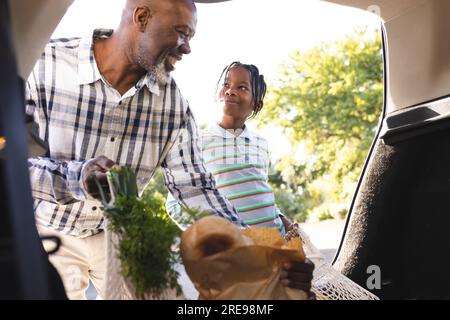 Fröhlicher afroamerikanischer Großvater und Enkel, der Lebensmittel ins Auto bringt Stockfoto