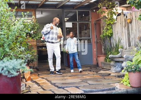 Glücklicher afroamerikanischer Großvater und Enkel, die Einkaufstüten in der Hand halten und den Supermarkt verlassen Stockfoto