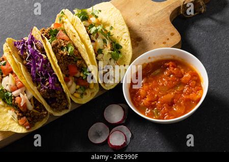 Blick aus einem hohen Winkel auf Tacos, serviert auf Holzbrett mit Soße in der Schüssel und Rettichscheiben auf dem Tisch Stockfoto