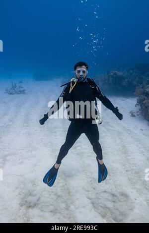 Ein ganzer Taucher trägt einen schwarzen Neoprenanzug und schwimmt unter Wasser mit Luftblasen und schaut auf den Meeresboden in Cancun in die Kamera Stockfoto