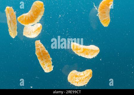 Nahaufnahme von tangerinen Segmenten, die ins Wasser fallen, mit Kopierraum auf blauem Hintergrund Stockfoto