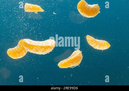 Nahaufnahme von tangerinen Segmenten, die ins Wasser fallen, mit Kopierraum auf blauem Hintergrund Stockfoto