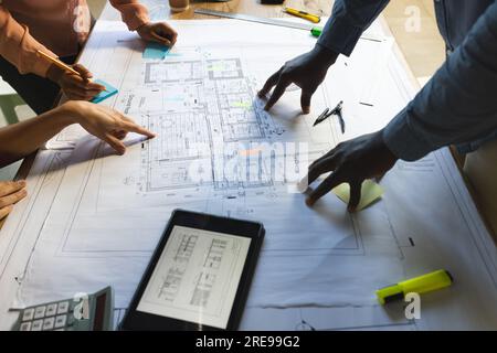 Verschiedene Kollegen diskutieren über die Arbeit mit einem Tablet über das Projekt, ein Büro zu bauen Stockfoto