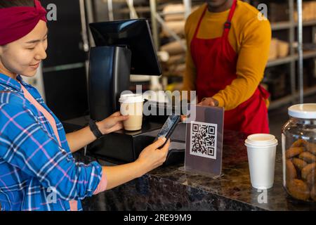 Zufriedener, vielseitiger männlicher Bäckereiarbeiter und Kunde, der qr-Code mit dem Smartphone scannt Stockfoto