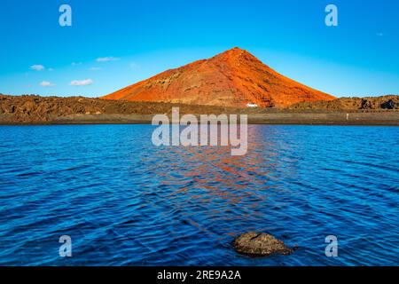 Ein roter Vulkan, der sich im blauen Wasser von playa de Janubio auf Lanzarote spiegelt Stockfoto