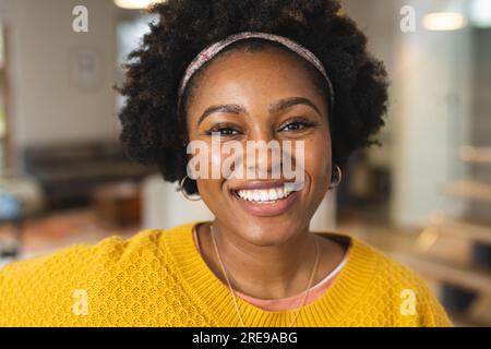 Porträt einer glücklichen afroamerikanischen Frau, die einen gelben, lächelnden Pullover trägt Stockfoto