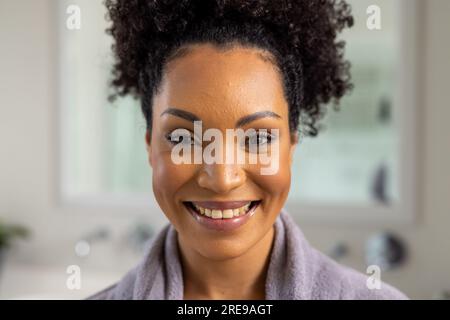 Porträt einer glücklichen birassischen Frau im Bademantel im Bad Stockfoto