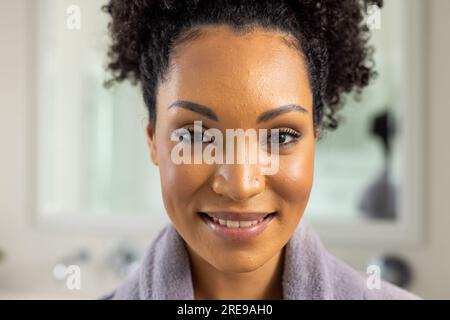 Porträt einer glücklichen birassischen Frau im Bademantel im Bad Stockfoto