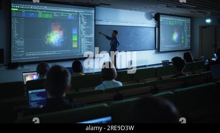 Junger männlicher Lehrer, der eine Vorlesung zur Datenwissenschaft für verschiedene ethnische Gruppen von weiblichen und männlichen Schülern im Dark College Room hält. Diashow Wird Projiziert Stockfoto