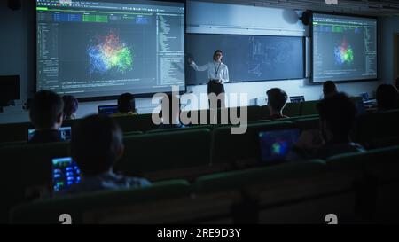 Junge Lehrerin, die eine Vorlesung zur Datenwissenschaft für verschiedene ethnische Gruppen von weiblichen und männlichen Schülern im Dark College Room hält. Diashow Wird Projiziert Stockfoto