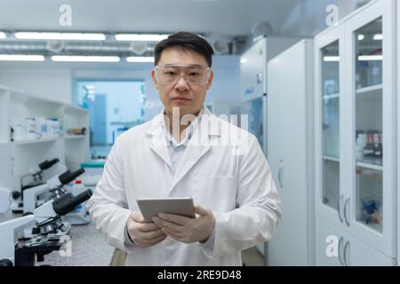 Porträt eines jungen asiatischen männlichen Wissenschaftlers im Labor mit Schutzbrille und Handschuhen. Er hatte einen Ordner mit Dokumenten in der Hand. Er schaut ernsthaft in die Kamera. Stockfoto