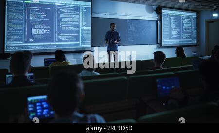 Junger männlicher Lehrer, der eine Vorlesung zur Datenwissenschaft für verschiedene ethnische Gruppen von weiblichen und männlichen Schülern im Dark College Room hält. Diashow Wird Projiziert Stockfoto