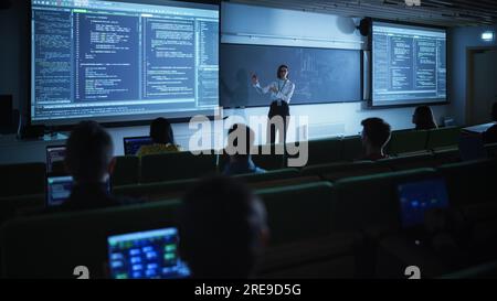 Junge Lehrerin, die eine Vorlesung zur Datenwissenschaft für verschiedene ethnische Gruppen von weiblichen und männlichen Schülern im Dark College Room hält. Diashow Wird Projiziert Stockfoto