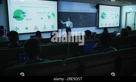 Junge Lehrerin, die eine Vorlesung zur Datenwissenschaft für verschiedene ethnische Gruppen von weiblichen und männlichen Schülern im Dark College Room hält. Diashow Wird Projiziert Stockfoto